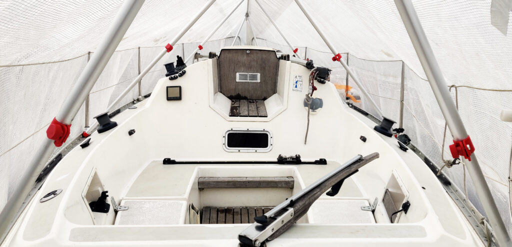 Purjeveneen kannella seisova metalliputkista koottu teline, jonka päällä on valkoinen pressu. 