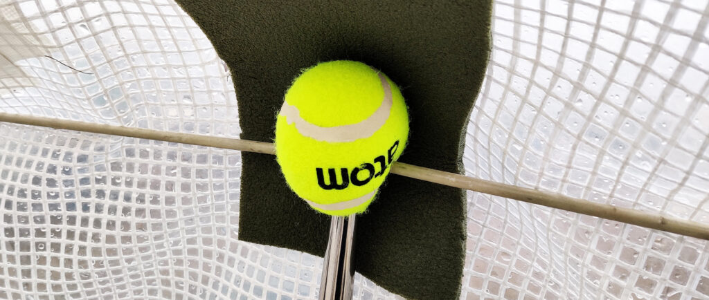 Keltainen tennsipallo kaidetolpan päässä, solumuovipala ja pressu. 