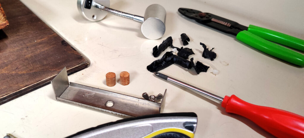 Elektroniikka-asennus alkaa purkamisella: Valkoisella pohjalla työkaluja, valaisin, tiikkitappeja ja muoviroskaa. 