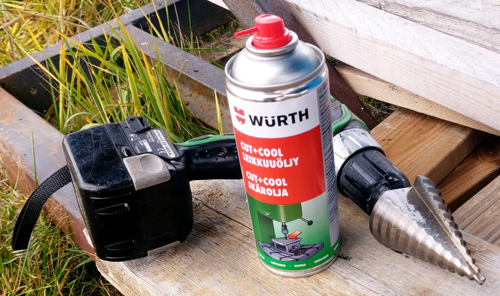 Akkuporakone, kartioterä ja leikkuuöljyä puisella alustalla.