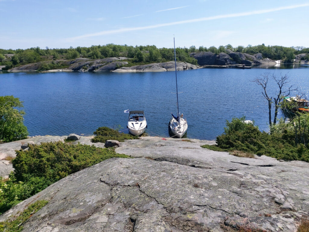 Kaksi purjevenettä kiinnitettynä kalliorantaan. Veneen moottoriongelmat ovat vasta edessäpäin.