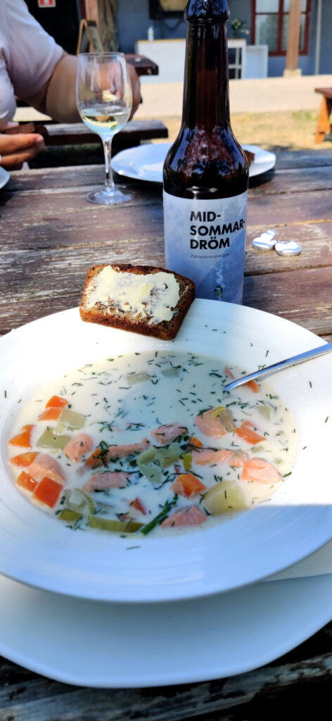 Kalakeitto, voideltu leipä ja olutpullo pöydällä auringonpaisteessa.