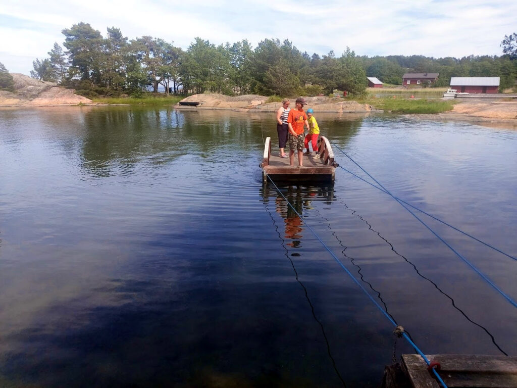 Puinen, vedettävä lossi tyynessä poukamassa. Moottorin sähköongelma unohtui hetkeksi. 