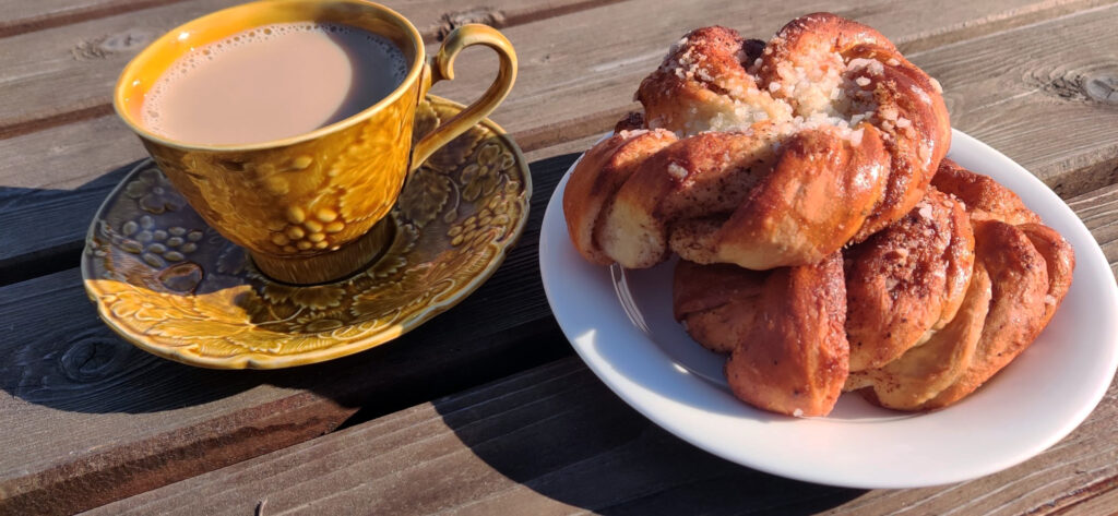 Keltainen kahvikuppi ja pullalautanen auringonpaisteessa.