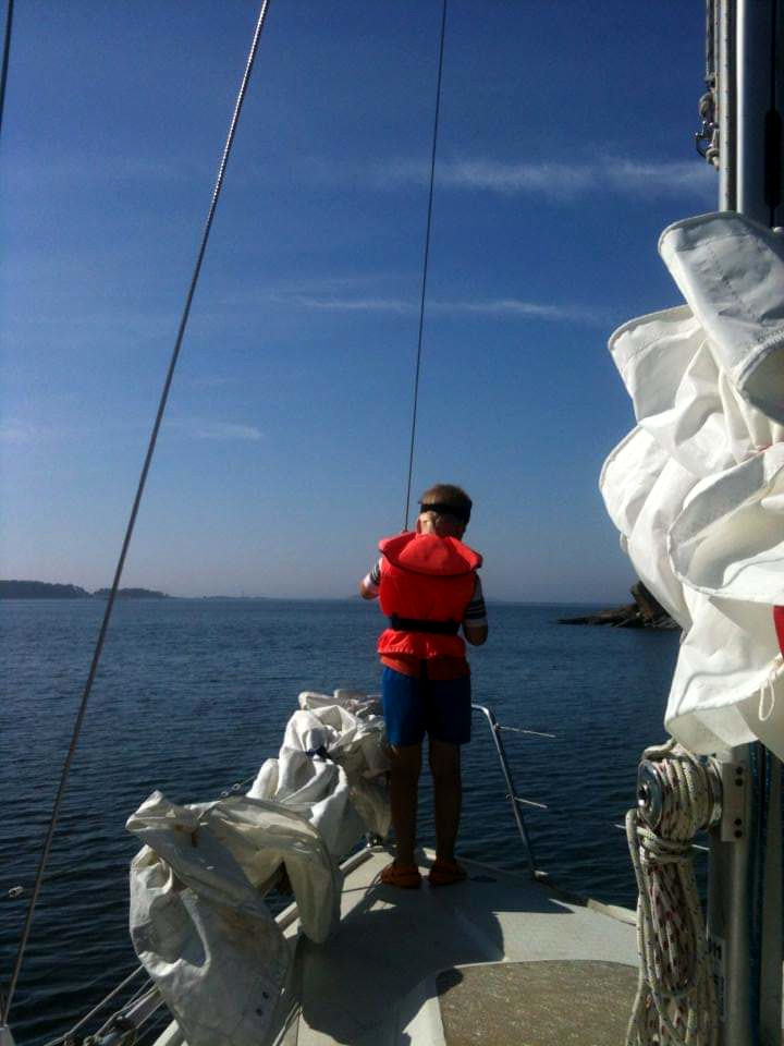 Lapsi purjeveneen keulalla, purjeet laskettuna