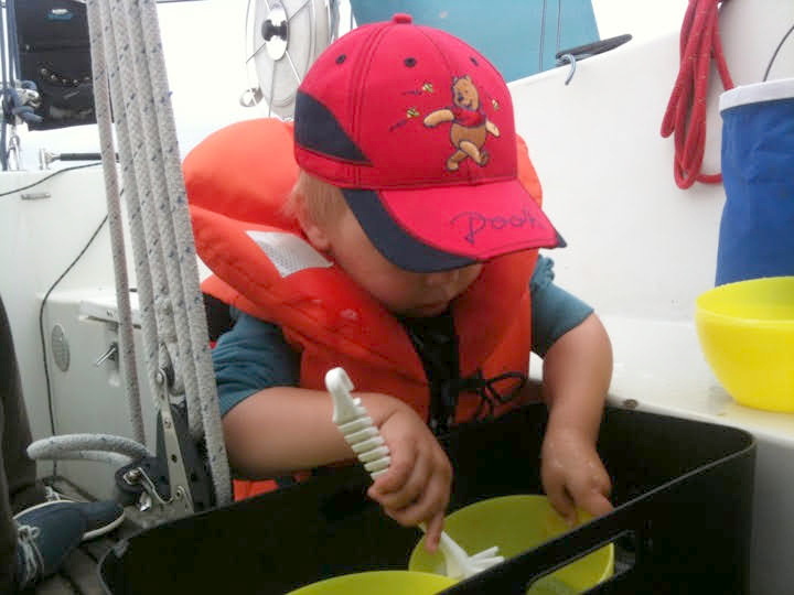 Lapsi tiskaa veneessä, punainen lippalakki päässä ja pelastusliivit päällä