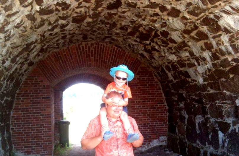 Pieni lapsi isänsä harteilla, kivimuurin aukossa