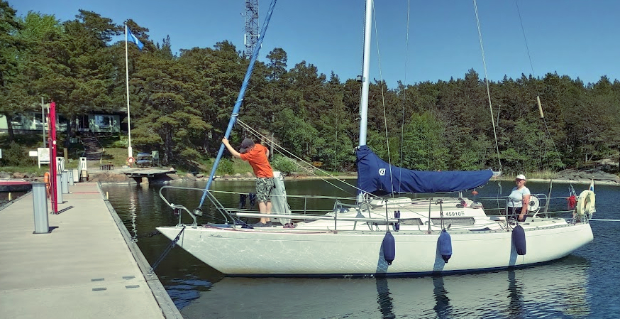 Purjevene laiturissa, lapsi kannella ja nainen avotilassa.