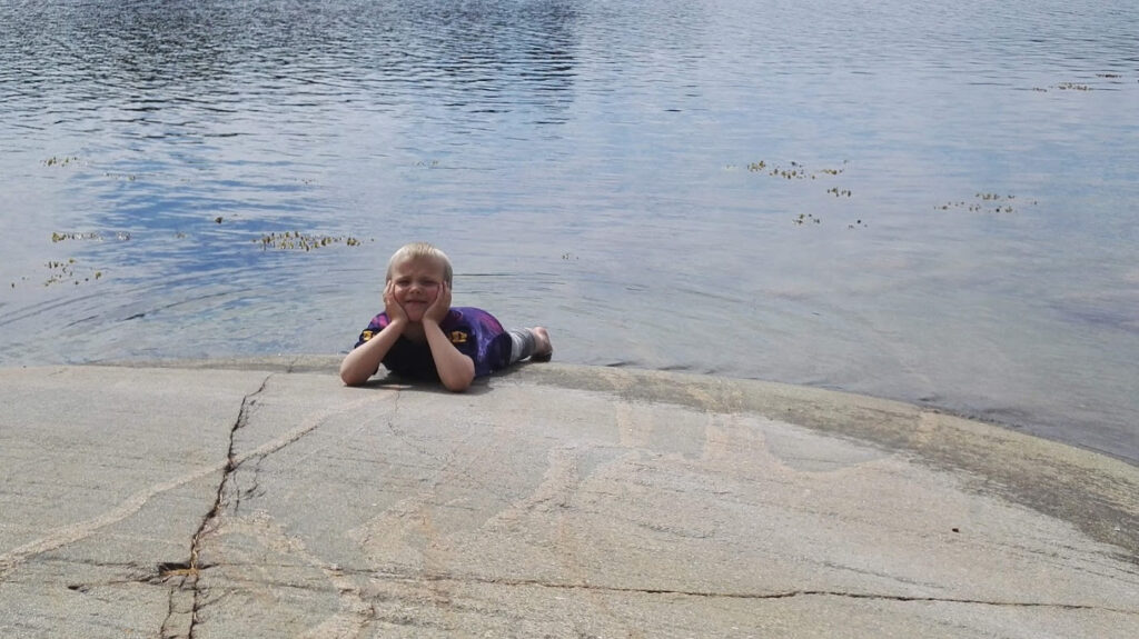 Lapsi nojaa leukaa käsiin ja makaa rantakalliolla