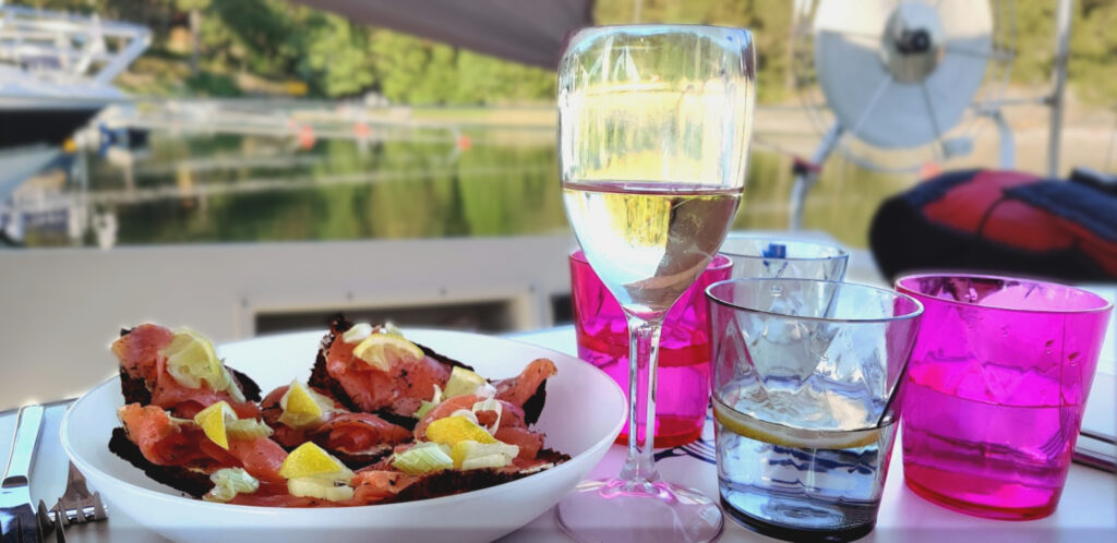 Lohileivät, viinilasi ja vesilasit veneen pöydällä, taustalla meri  ja Bodö -saaren rantakallio