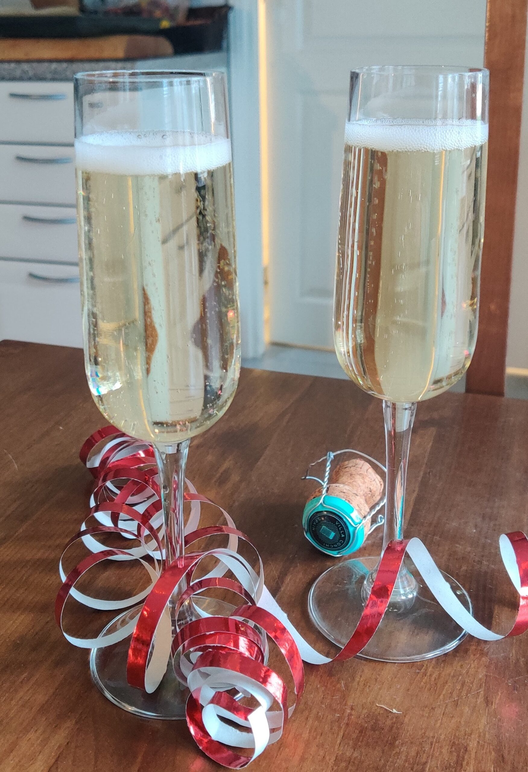 Kaksi kuohuviinilasia, serpentiiniä ja kuohuviinipullon korkki pöydällä