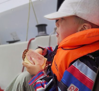 Lapsi istuu purjeveneen istumakaukalossa leipä kädessään