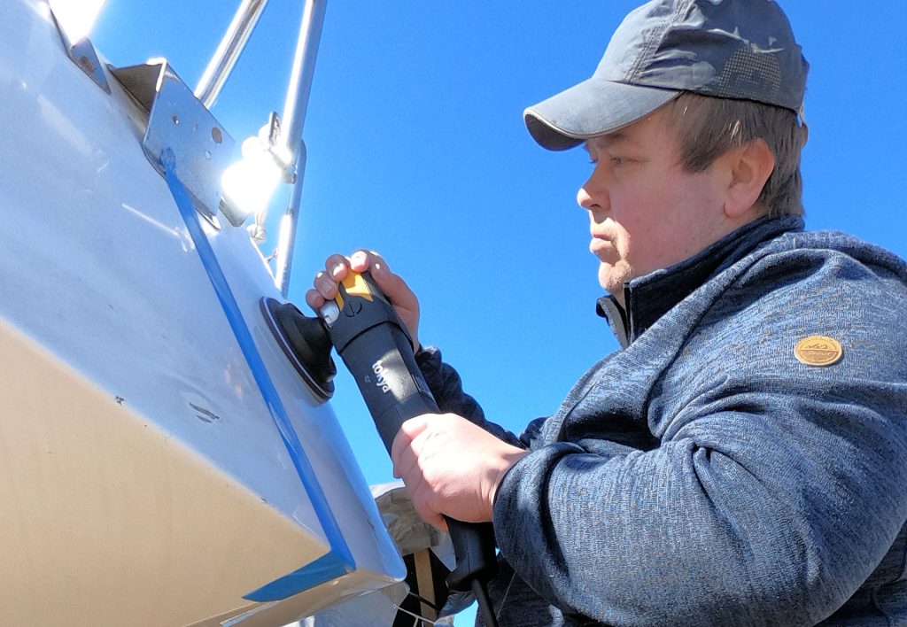 Kapteeni lippis päässä keskittyneesti kiillottamassa purjeveneen peräpeiliä.